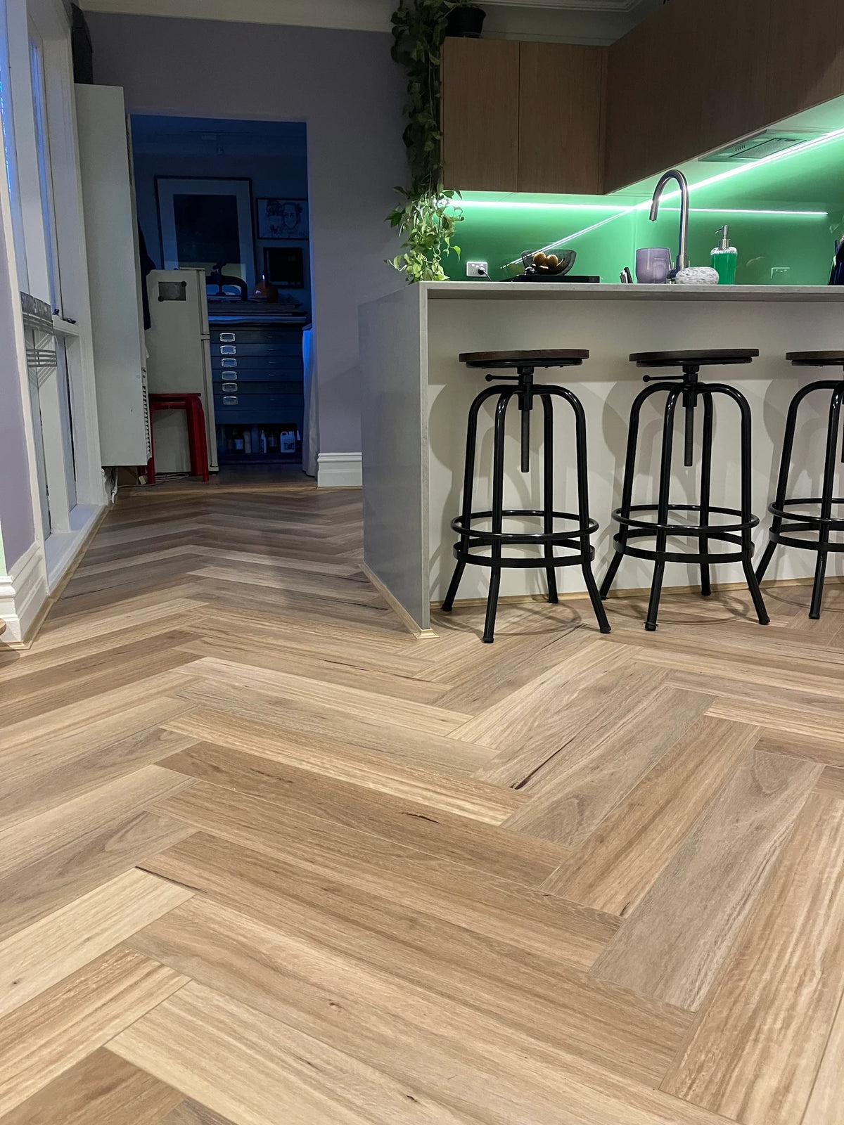 Coastal Blackbutt hybrid flooring in a herringbone pattern. Durable, waterproof planks with a realistic wood grain finish.